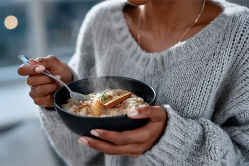 Woman enjoying a warm bowl of oatmeal topped with cinnamon, a powerful anti-inflammatory spice that supports gut and immune health.