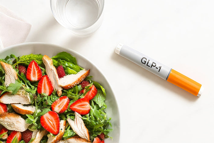 A balanced meal of lean protein and produce sits beside a GLP-1 injector, highlighting the importance of nutrition alongside medication in obesity care.