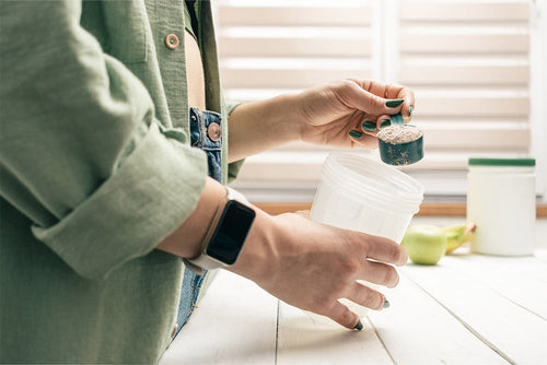 A person scooping protein powder into a shaker bottle, representing HMB supplementation for muscle recovery, strength, and performance support.