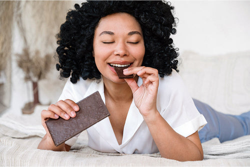 A woman relaxes while savoring a bar of chocolate, highlighting the irresistible pull of sugar and its impact on cravings.