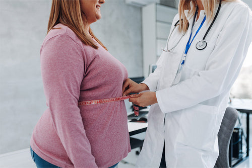A clinician measures a patient’s waist circumference, emphasizing the importance of monitoring body composition in obesity care and treatment planning.