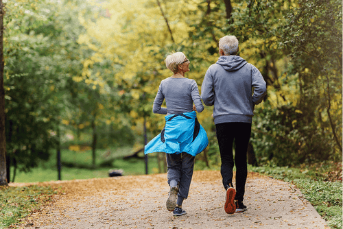 An older couple jogging through a park, representing recovery, mobility, and improved outcomes supported by proper perioperative nutrition.