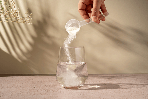 A hand pours HMB powder into a glass of water.