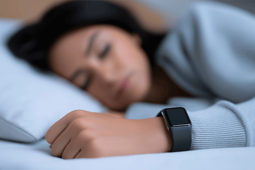 Person sleeping while wearing a smartwatch that tracks sleep data, illustrating how wearable technology measures sleep as a key health metric.
