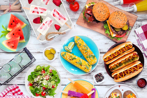 Colorful summer BBQ spread with burgers, hot dogs, salad, fruit, grilled corn, and popsicles, reflecting how health experts balance classic cookout favorites with fresh, nourishing foods.