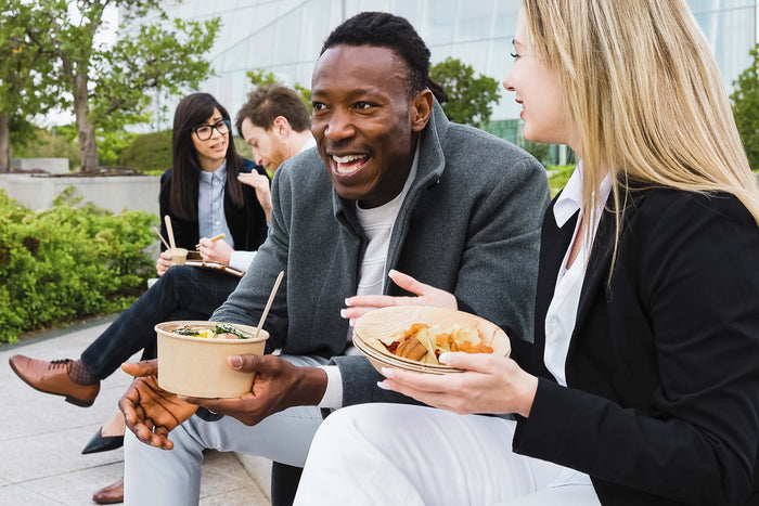 Colleagues sharing a meal together outdoors, highlighting the connection between social health, physical wellbeing, and everyday nutrition.