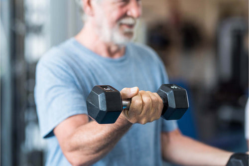 Older man smiling while lifting a dumbbell, showing how strength training supports muscle health.