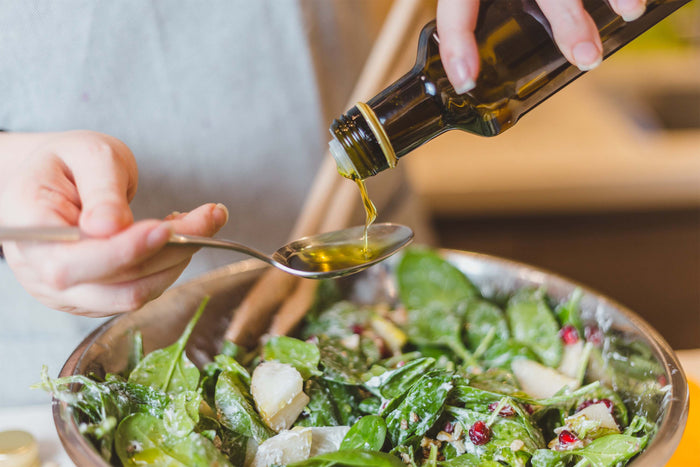 Olive oil is poured over a fresh spinach salad, highlighting a simple and flavorful way to add heart-healthy fats.