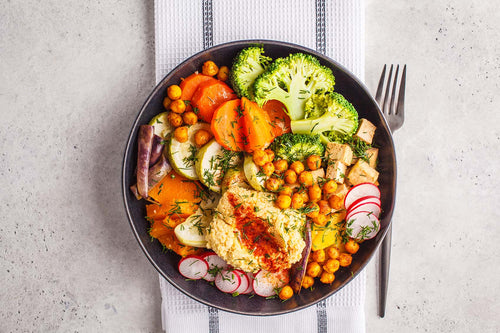 A colorful lettuce-free salad bowl featuring roasted vegetables, chickpeas, tofu, hummus, and radishes offers a nutritious alternative during the produce outbreak.