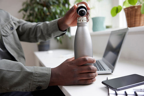 Person pouring water into a reusable bottle indoors, highlighting the importance of staying hydrated during winter months when thirst cues are often reduced.
