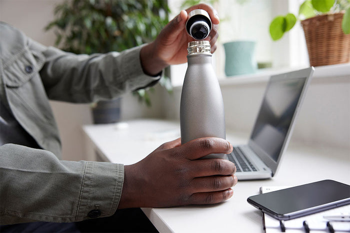Person pouring water into a reusable bottle indoors, highlighting the importance of staying hydrated during winter months when thirst cues are often reduced.